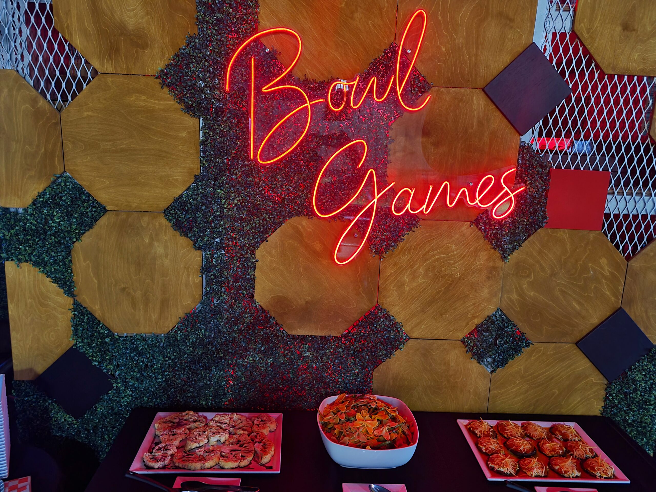 Neon eats & tasty treats! BowlGames sign shines on a table full of food.