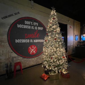 Holiday lights & inspirational vibes: BowlGames wall says "Don't cry because it's over, Smile because it happened!" with a bright Christmas tree.